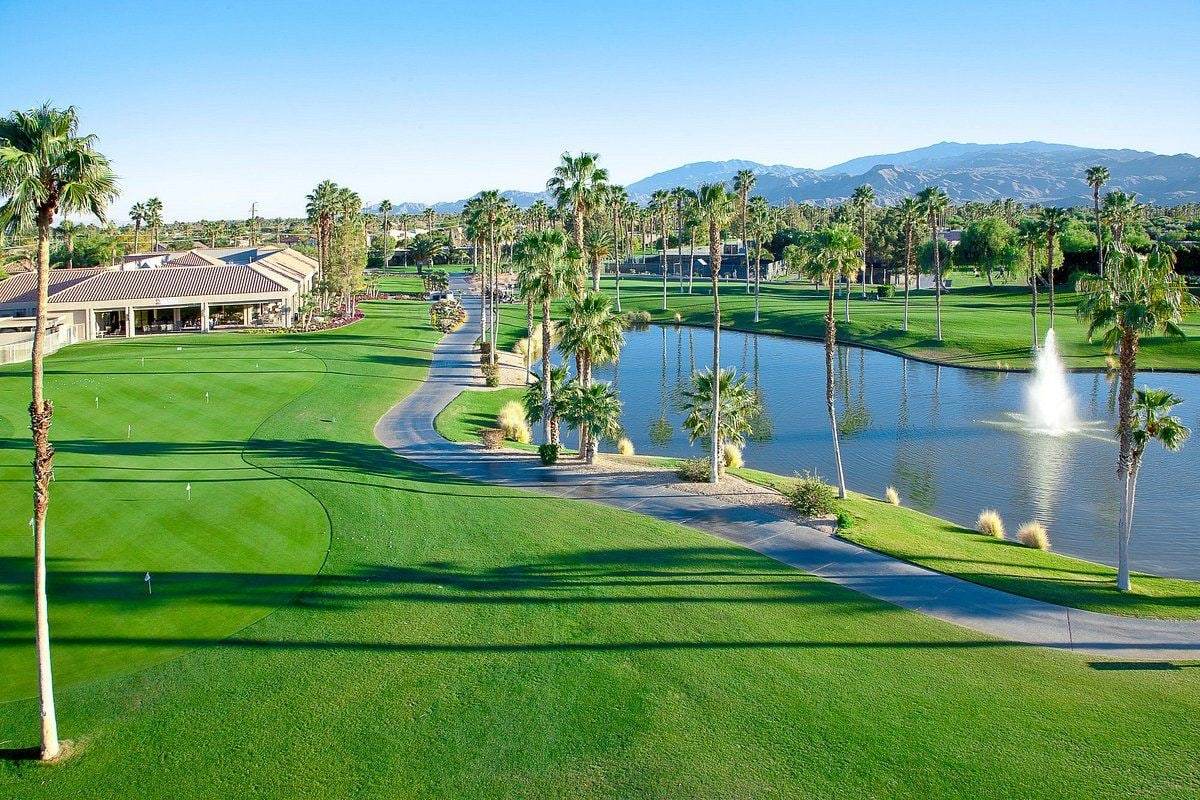 Desert Princess clubhouse beside a fairway, and a pond with a fountain, with the mountains beyond