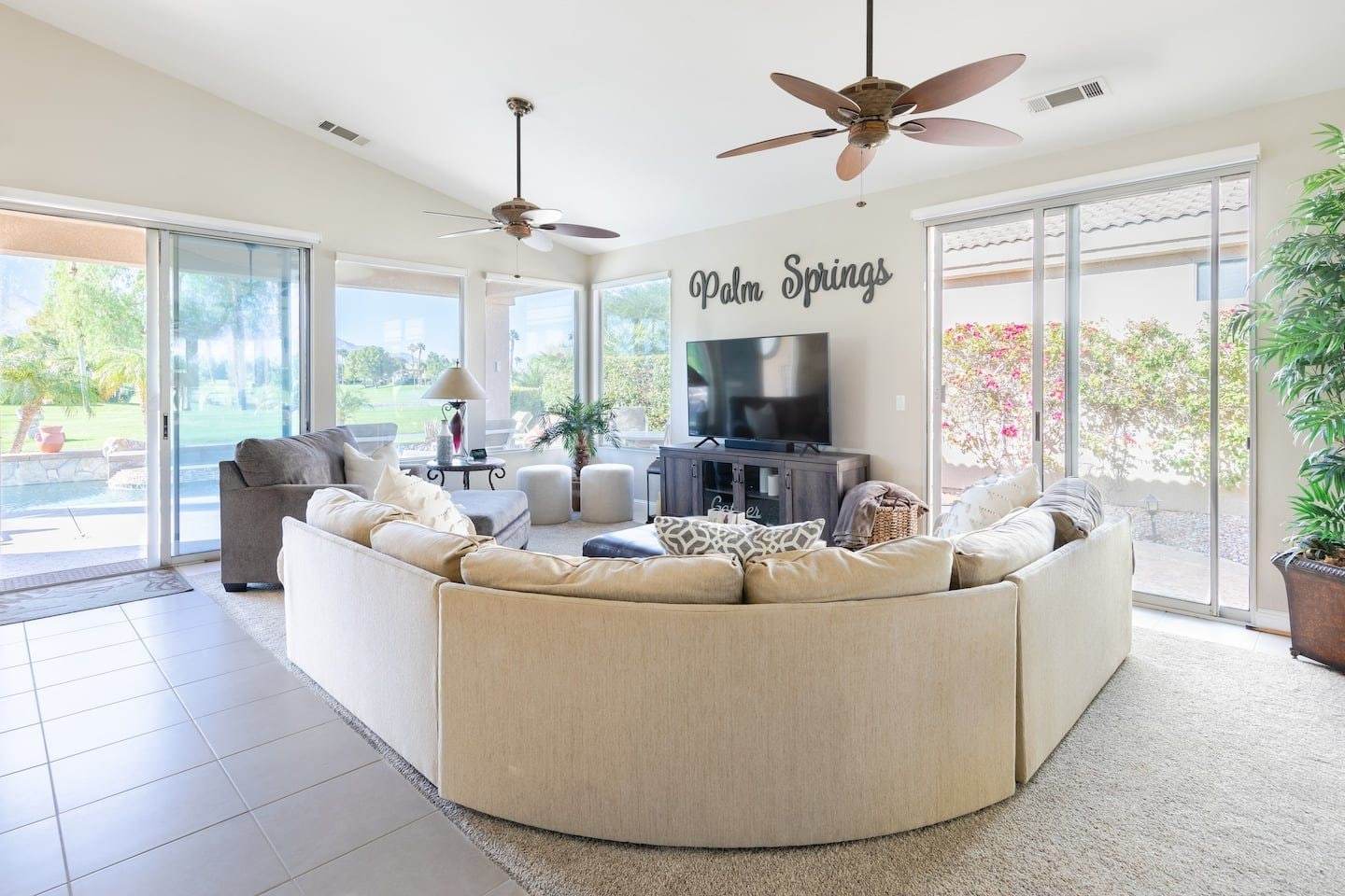 Living room with a curved cream sectional, white poufs and sliding glass doors to the pool