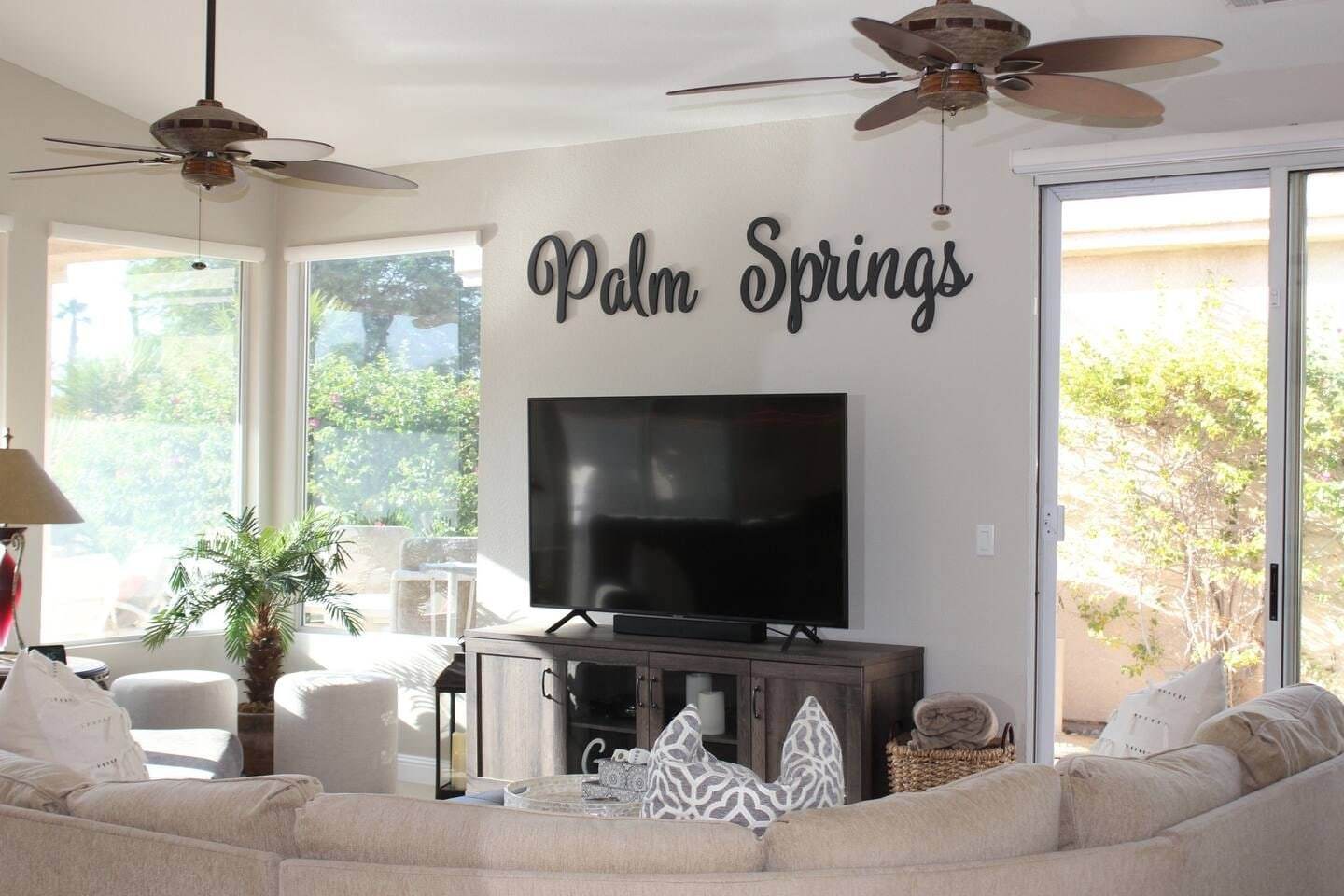 TV on a wood console under Palm Springs wall lettering, with the sectional in front