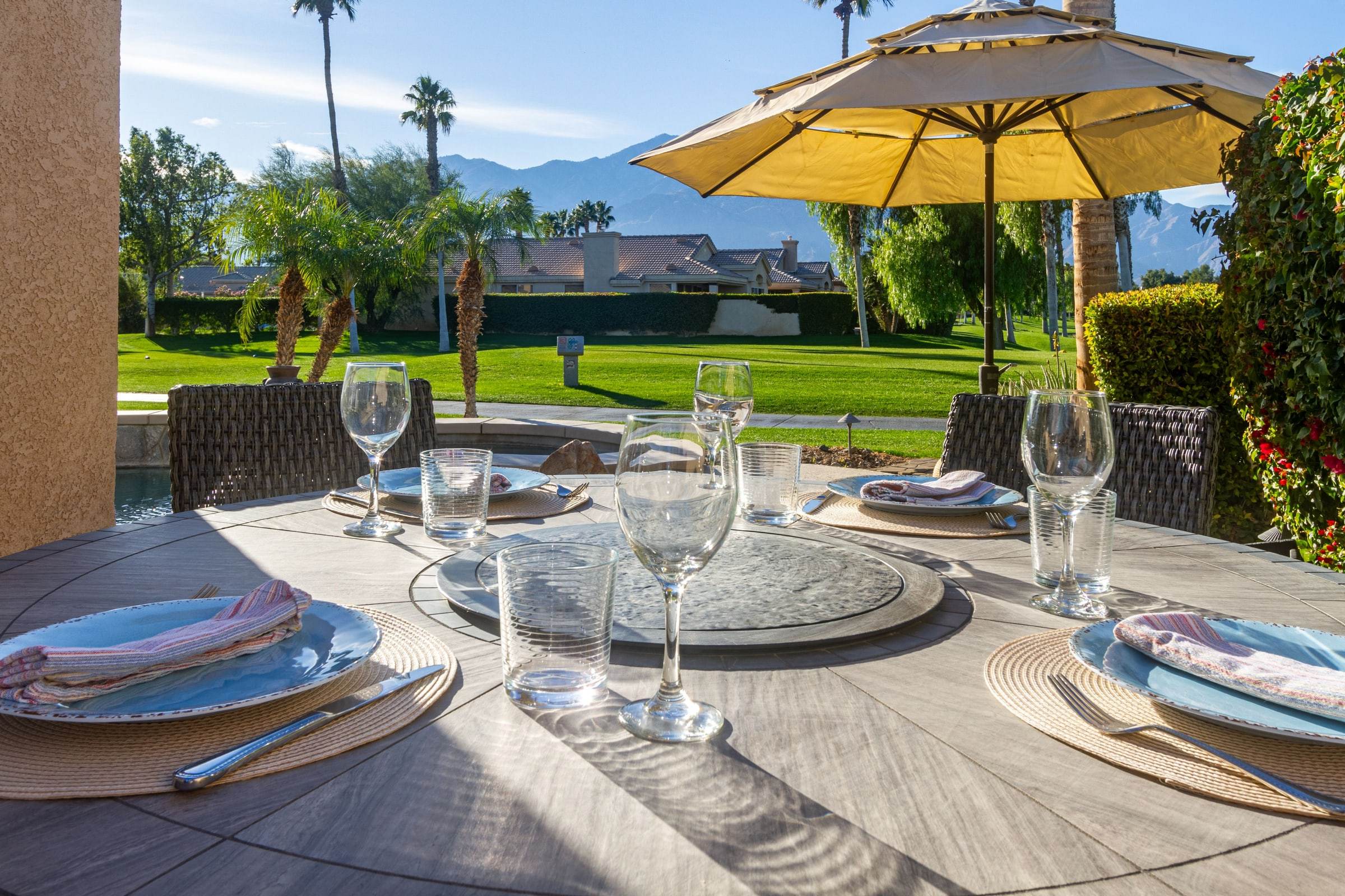 Round patio table set for dinner beside the pool, with the fairway, palms and mountains beyond