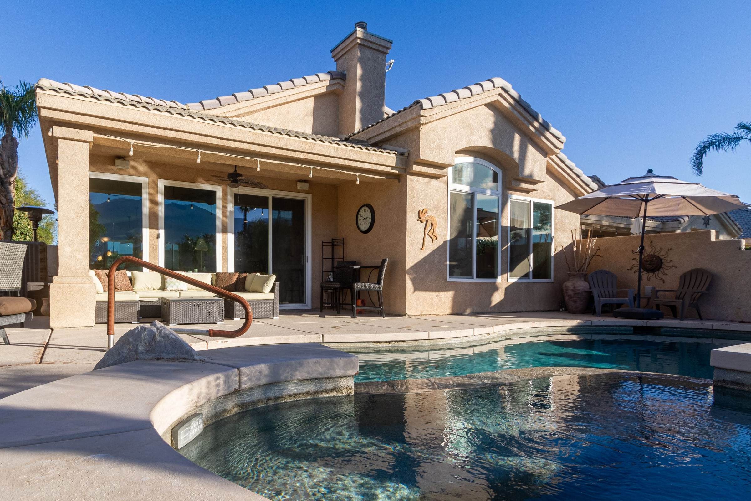 Back of the house: covered patio with a sectional, two Adirondack chairs, and the pool and spa in front