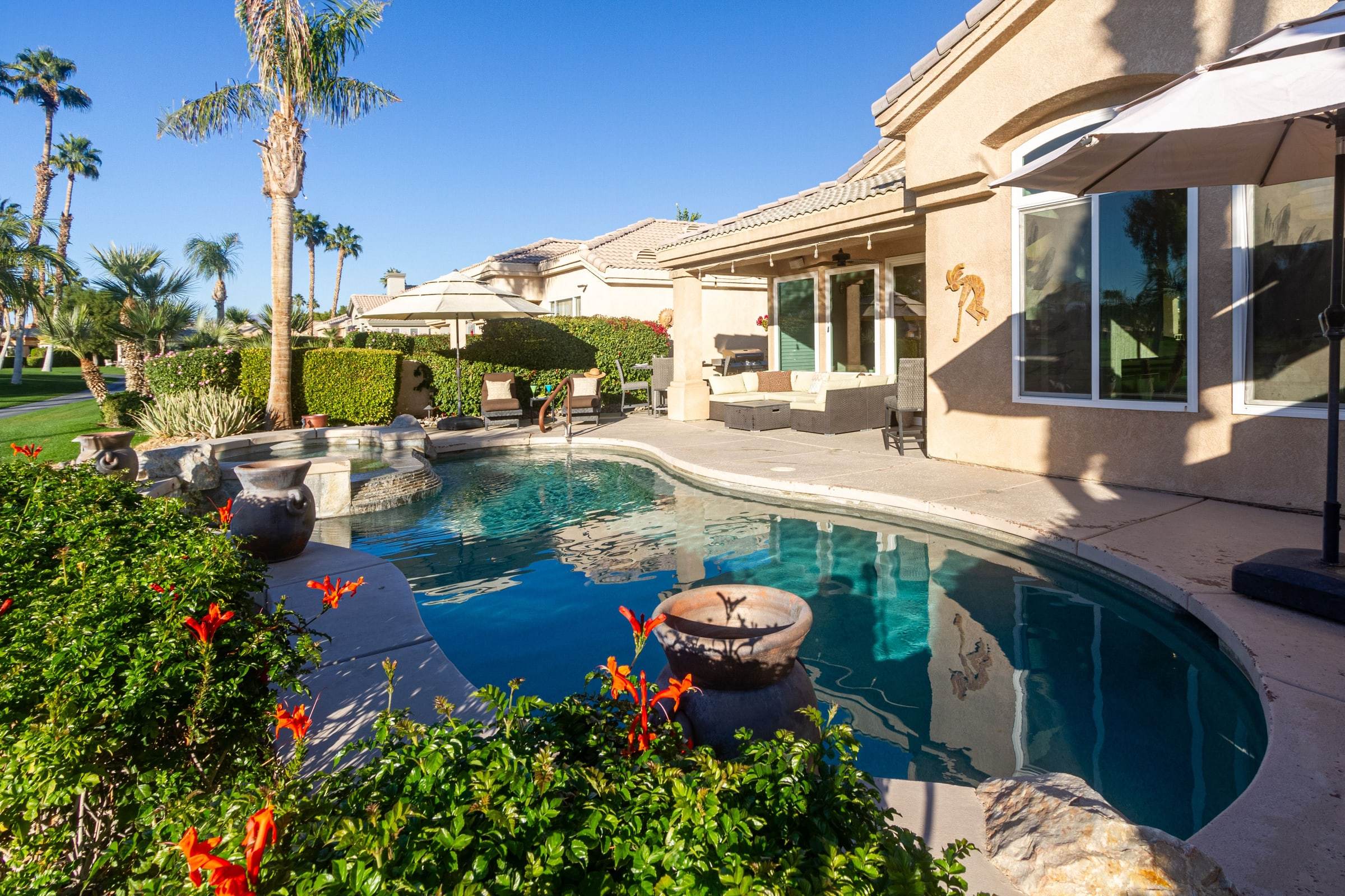Pool with orange flowers in the foreground and the back of the house and covered patio on the right