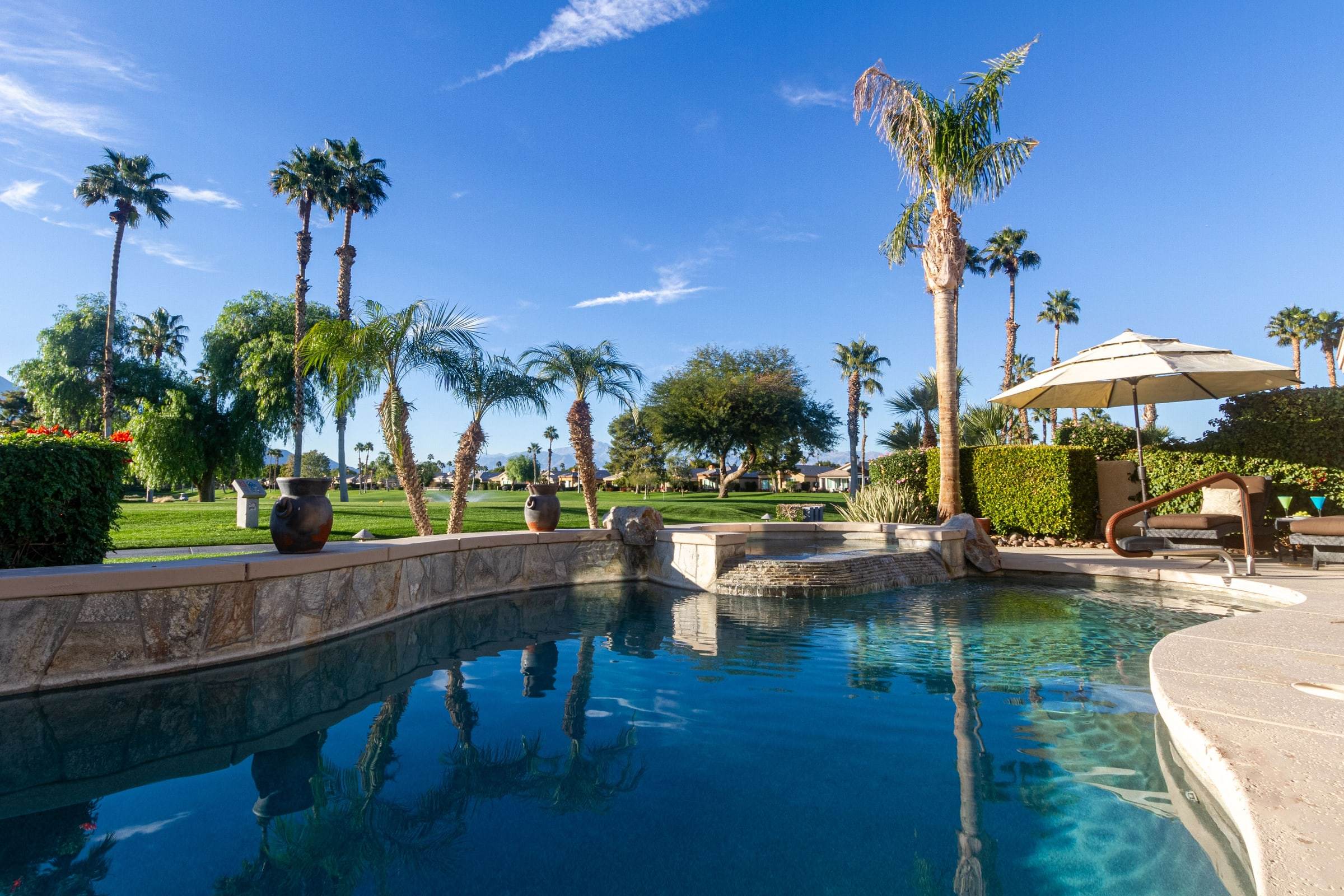 Pool, stone wall and spa, with a lounger under an umbrella on the far side