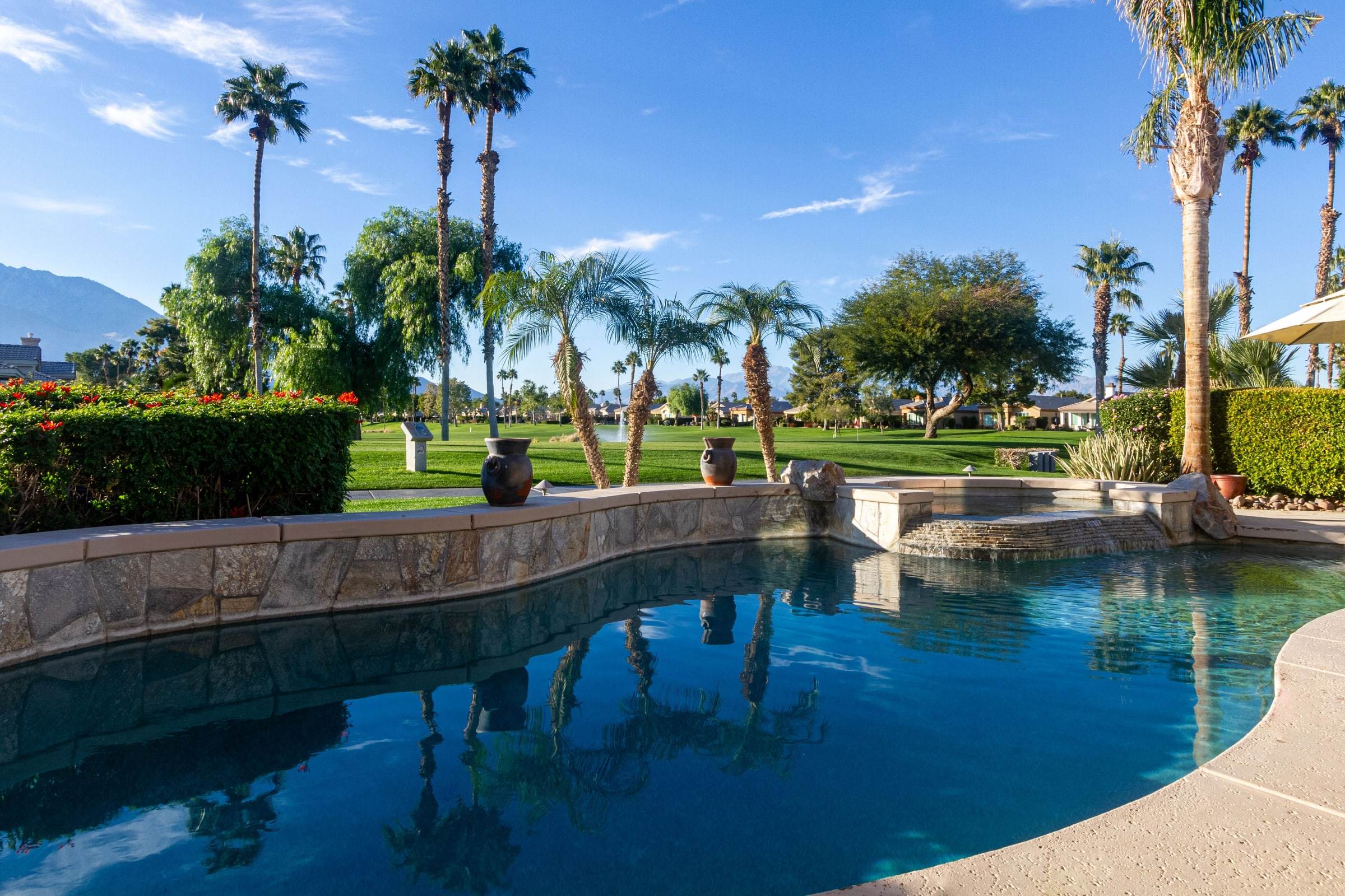 Pool, stone wall and spa waterfall, with palms and the fairway beyond