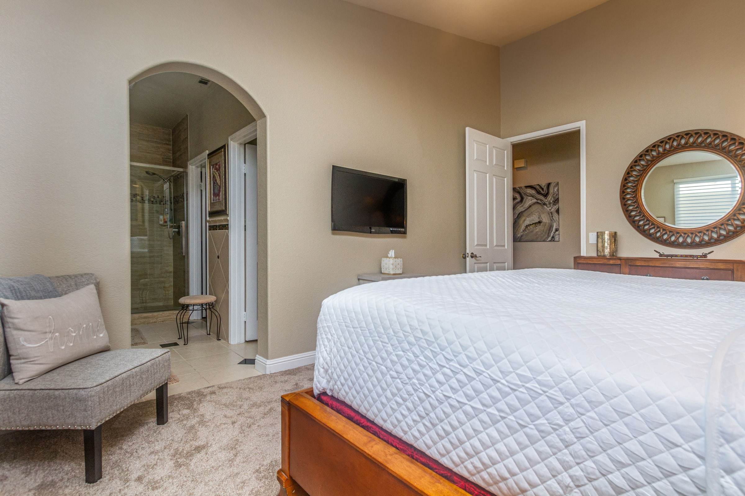 Primary bedroom with a wall TV, a dresser and an arched doorway to the bathroom