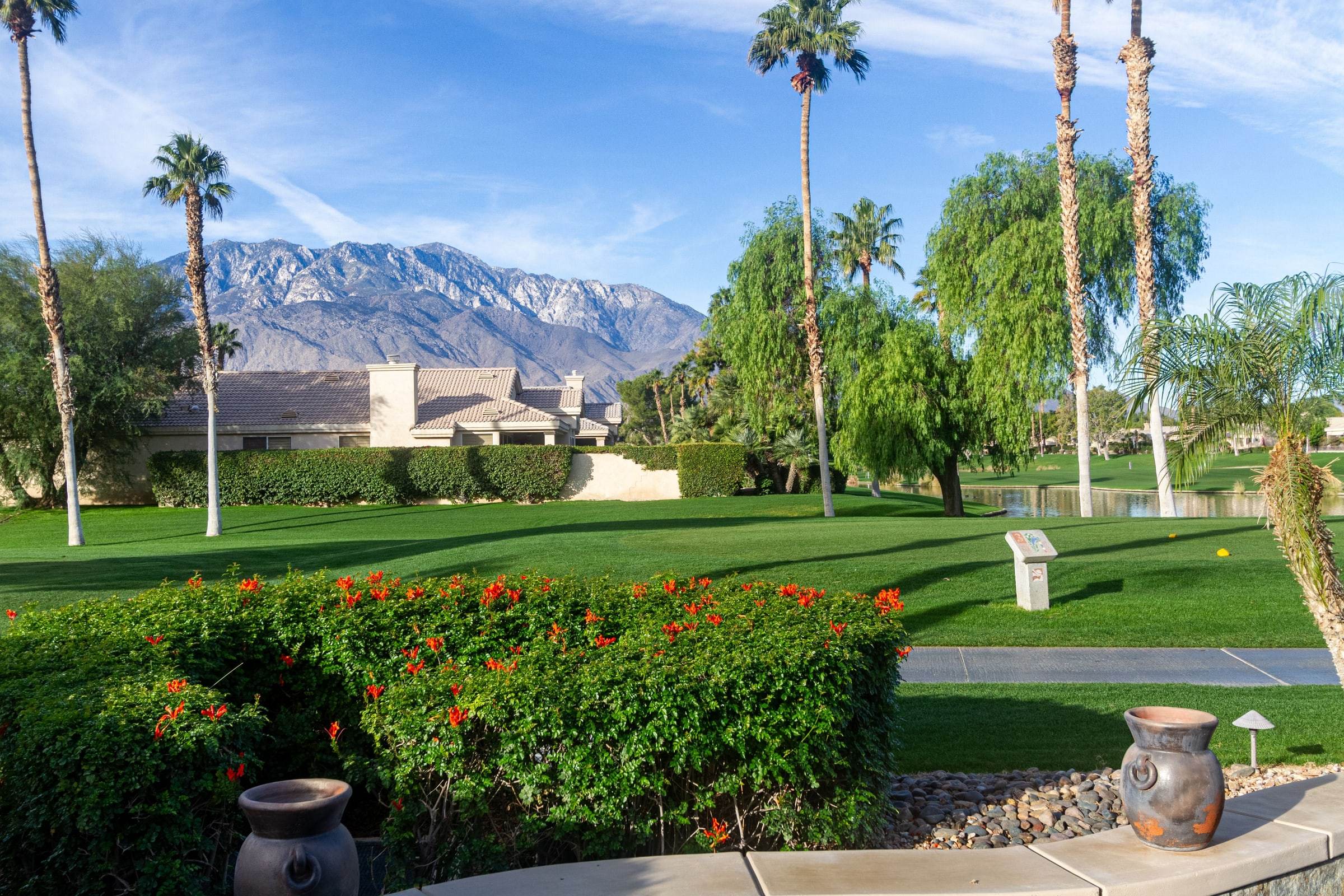 Red flowering hedge and urns framing the golf course and mountains